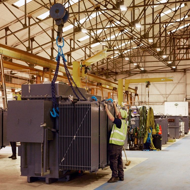 distribution transformer lifted on a crane in a workshop